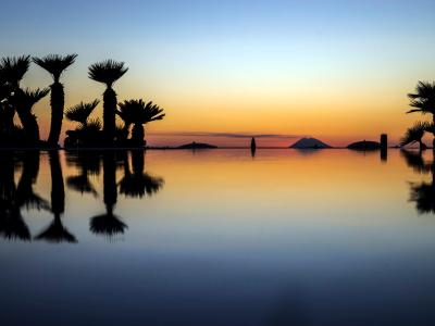 Tramonto tropicale con palme riflesse in acqua calma.