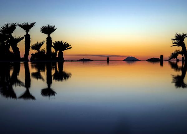 Tramonto tropicale con palme riflesse in acqua calma.