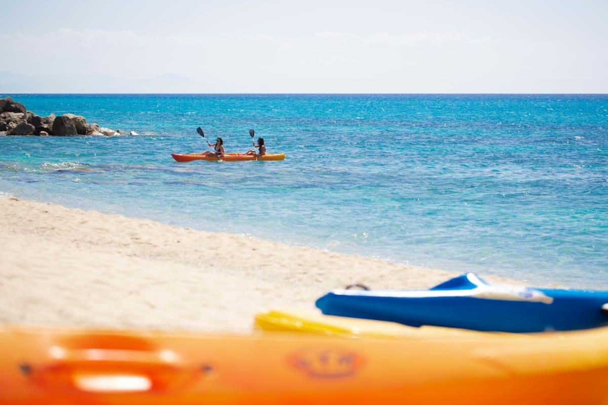 Zwei Personen im Kajak auf blauem Meer mit Sandstrand.