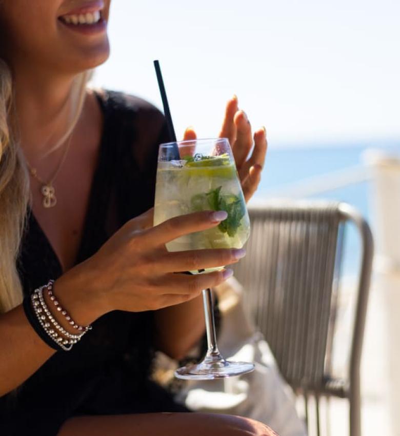 Lächelnde Frau mit Cocktail am Strand, sonniger Tag.