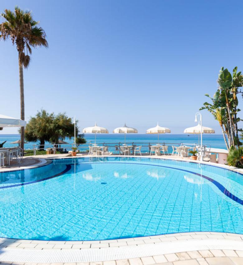 Pool mit Meerblick, Palmen und weißen Sonnenschirmen.