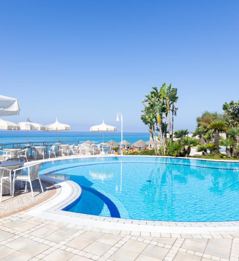 Pool mit Meerblick, weiße Stühle und Sonnenschirme.