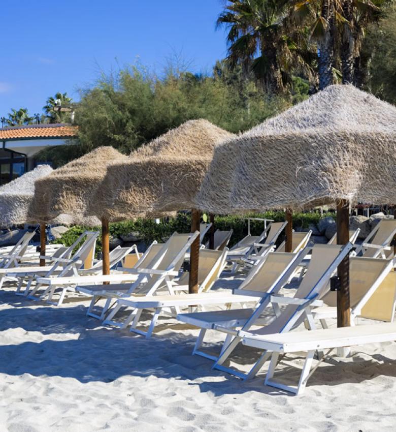 Plage avec transats et parasols en paille, palmiers en arrière-plan.