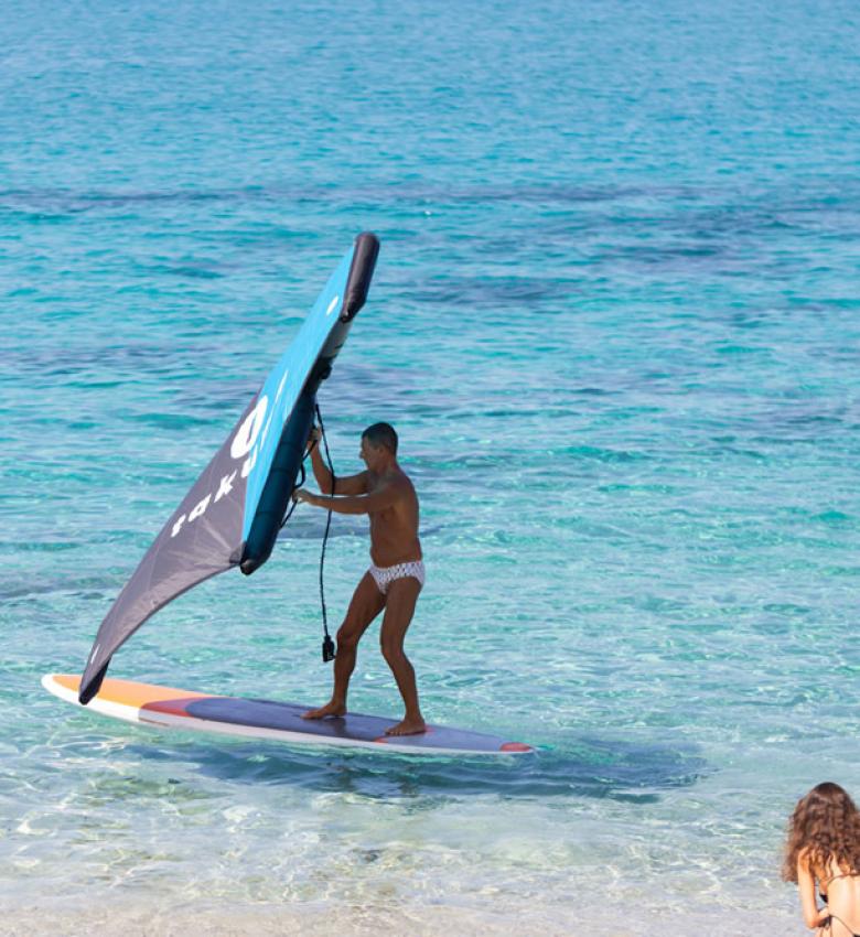 Homme fait de la planche à voile, deux femmes regardent sur la plage.
